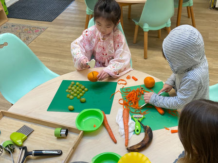 Children preparing cut grapes, peeled carrots and squeezed oranges for snack time at Treetops Montessori Preschool