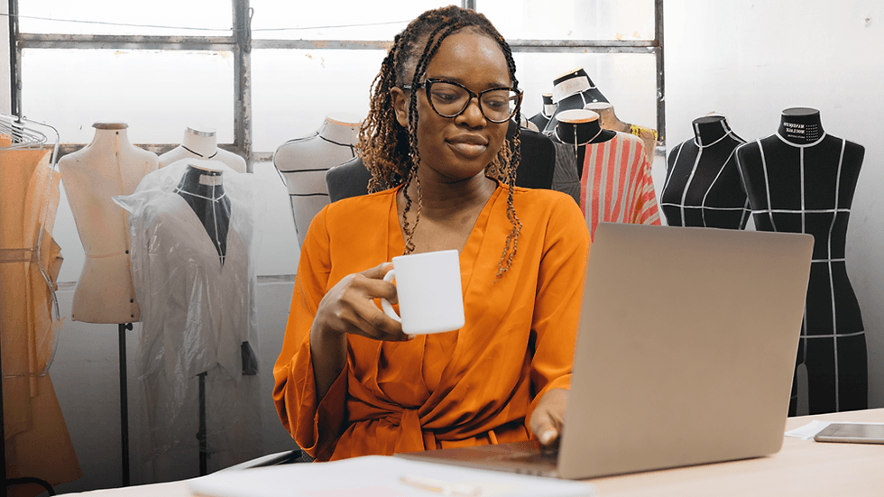 Fashion retail professional working on a laptop to manage product data in a studio with clothing mannequins