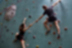 Two climbers reach for each other mid-ascent — seizing the moment, moving upward, and refusing to wait.