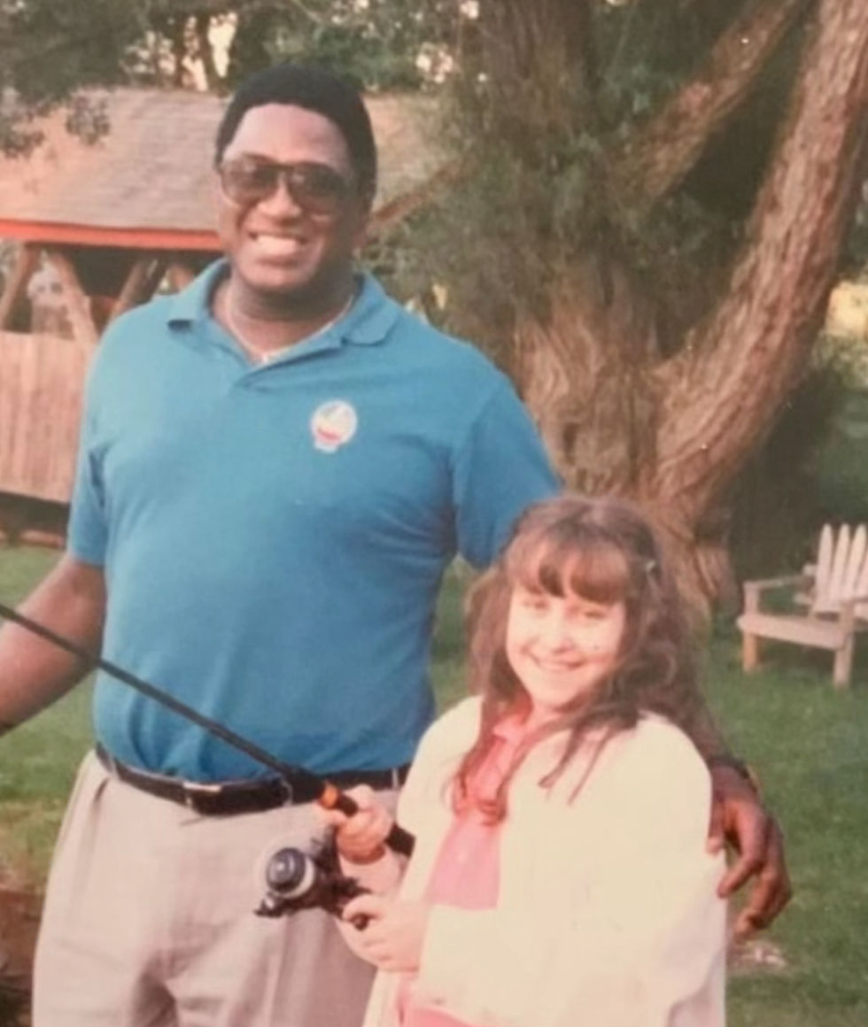 Smiling man in blue polo and sunglasses stands with a young girl holding a fishing rod in a backyard by a tree.
