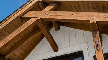 Wooden timber roof trusses on a white house exterior.