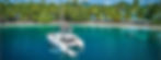 Luxury catamaran sailing along a palm-fringed white sand beach in French Polynesia during a premium bareboat yacht charter.