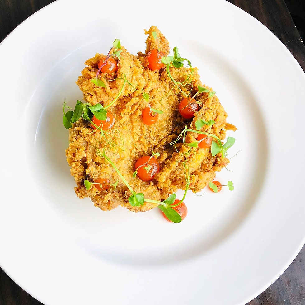 Crispy fried food topped with cherry tomatoes and greens on a white plate, set against a dark background, creating a fresh and vibrant look.