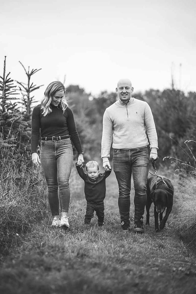A family walking hand in hand though trees with their dog.