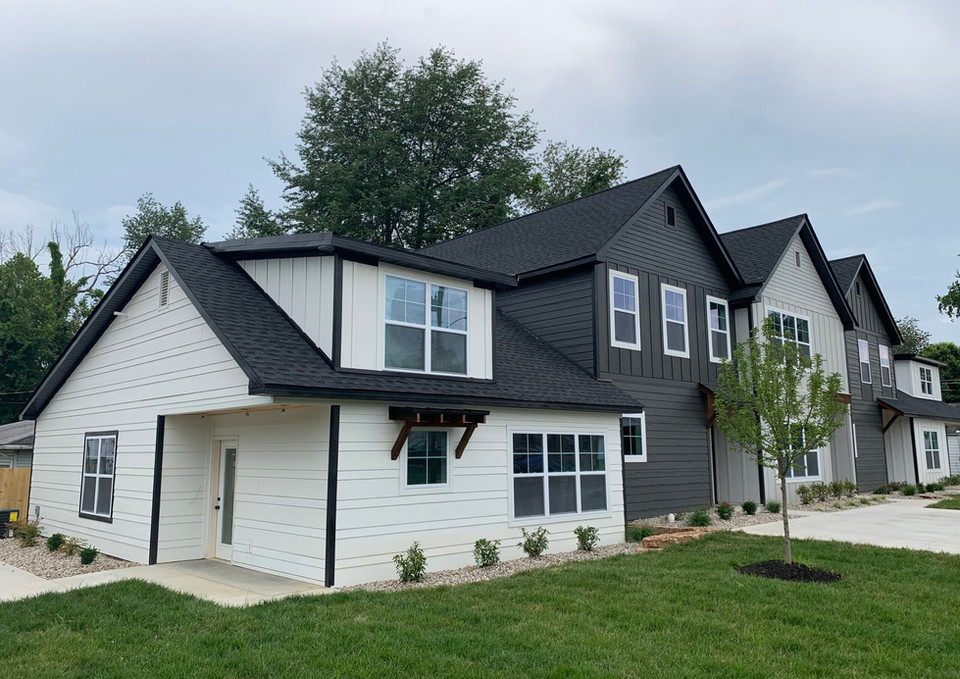 Modern townhouses with black and white exterior with lush green lawn and trees.