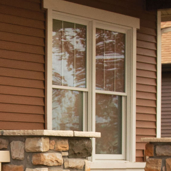 White window frame on brown siding with stone foundation, exterior view.