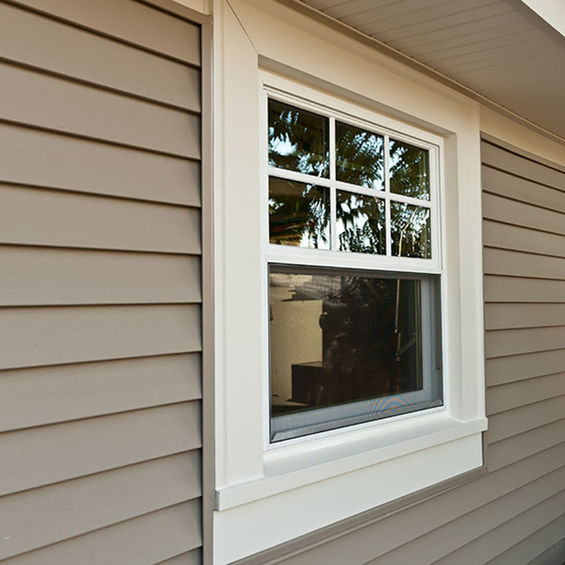 White framed window on a beige house, reflecting trees outside.
