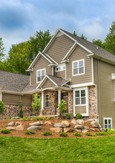 Two-story modern home with stone accents and a manicured lawn, surrounded by trees.