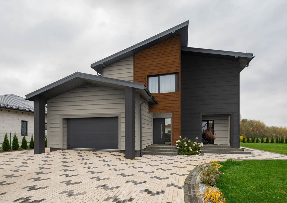 Modern home exterior with gray siding, garage door, and a patterned driveway.