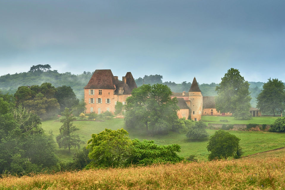 Chateau surrounded by rolling green hills and mist in France.