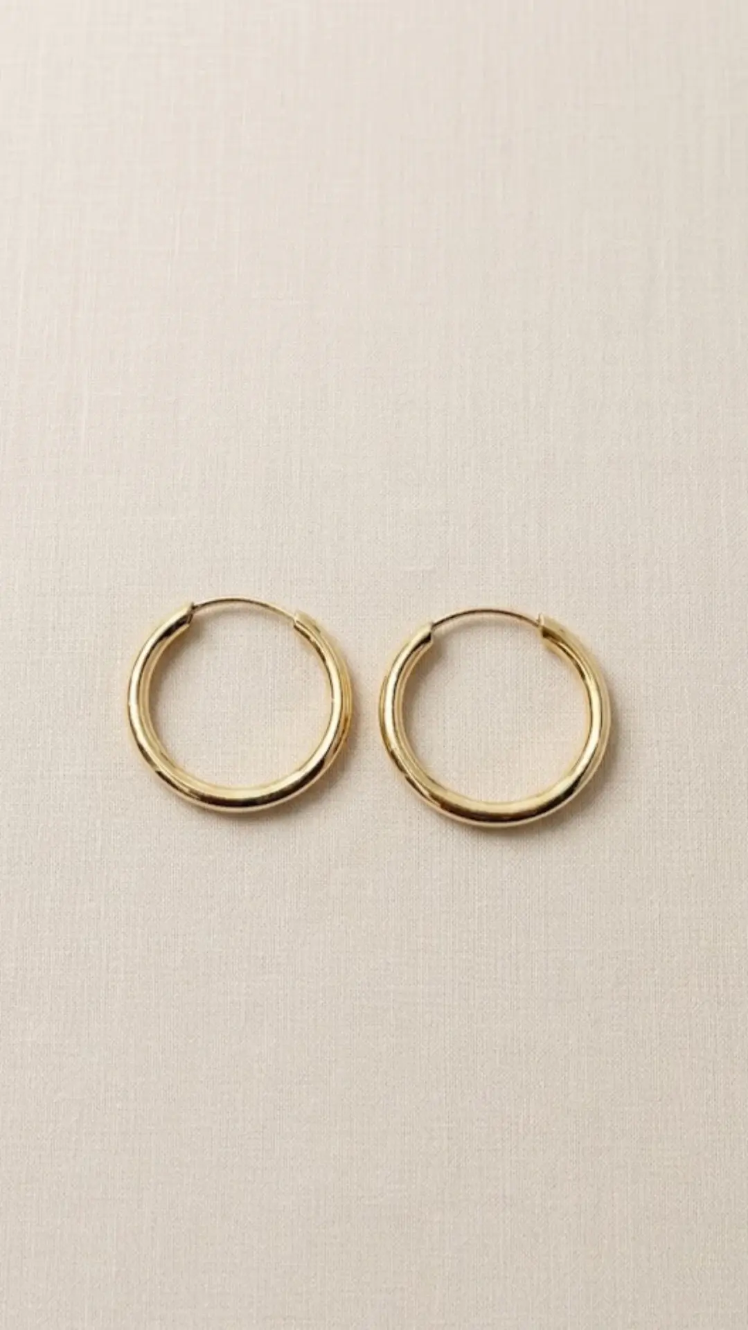 Un par de argollas clásicas lisas de oro amarillo de 18k sobre una superficie de lino blanco con textura.
