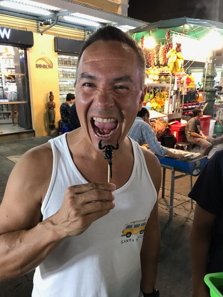 Peter eating a scorpion on a stick at a night market in Bangkok.
