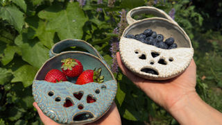 Two handmade ceramic berry bowls held outdoors, filled with fresh strawberries and blueberries.