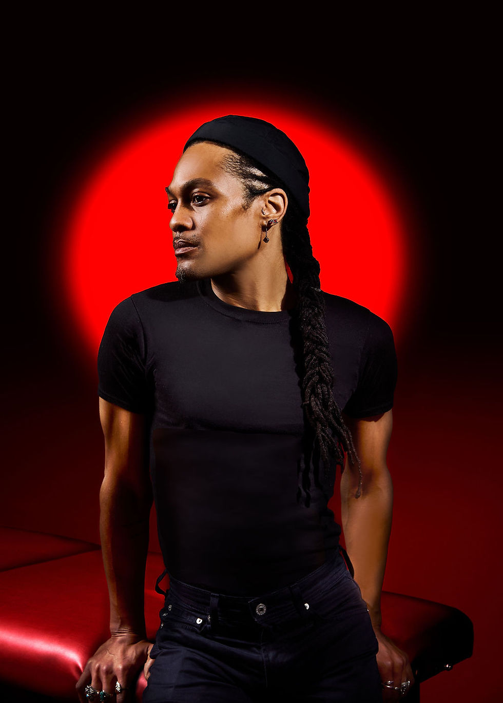 Man with long braid in black shirt against red circle