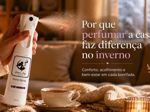 Uma sala de estar aconchegante em tons quentes (manta sobre o sofá, luz amarelada, talvez uma xícara de chá por perto), com o Home Spray Lunna Luz em primeiro plano sendo borrifado no ar, sugerindo o ritual de perfumar a casa em um dia frio.