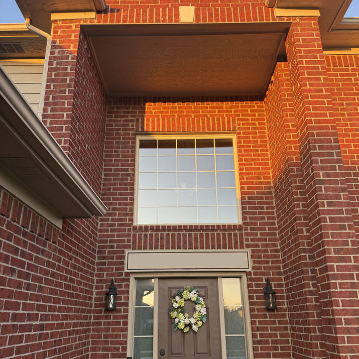 Residential window cleaning service in Macomb Michigan for a tall entryway window on a brick home, resulting in a streak-free shine. Clean second-story window after a professional cleaning/washing service