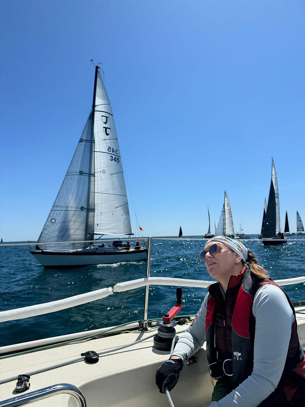 A woman looking up at sails in a race with other sailboats around