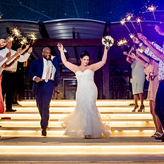 A newlywed couple joyfully walks down illuminated steps as friends and family celebrate with sparklers, creating a magical and unforgettable wedding night moment.