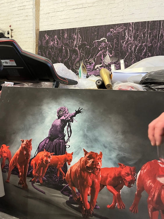 Art prints in Mary Sibande’s studio show a figure in purple and red dogs against a smoky backdrop. Abstract purple design in the background.
