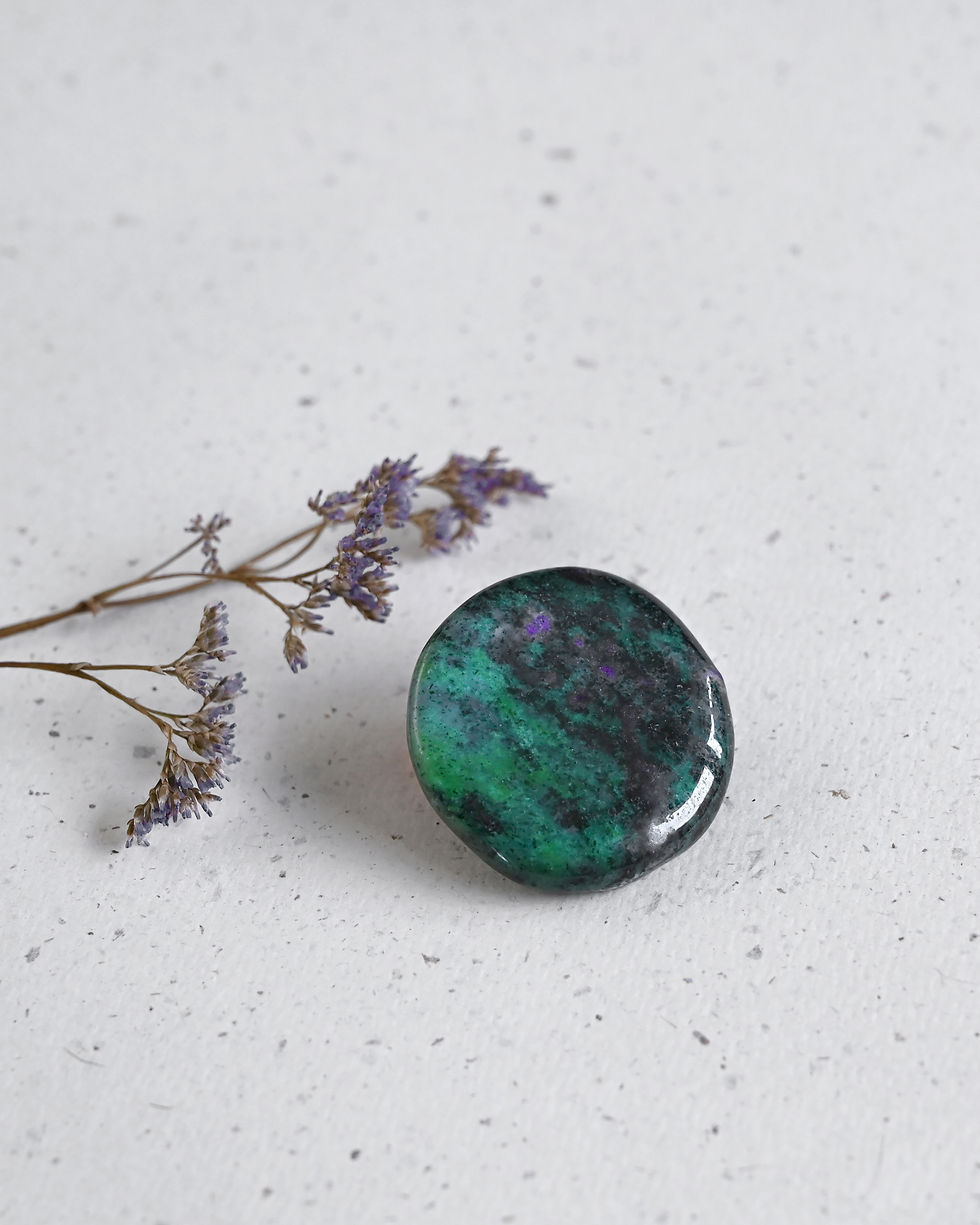 Glanzende groene en paarse Robijn in Zoïeciet naast gedroogde paarse bloemen op witte ondergrond.