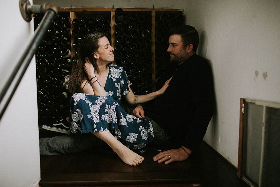 Couple sits on staircase in front of wine bottle collection