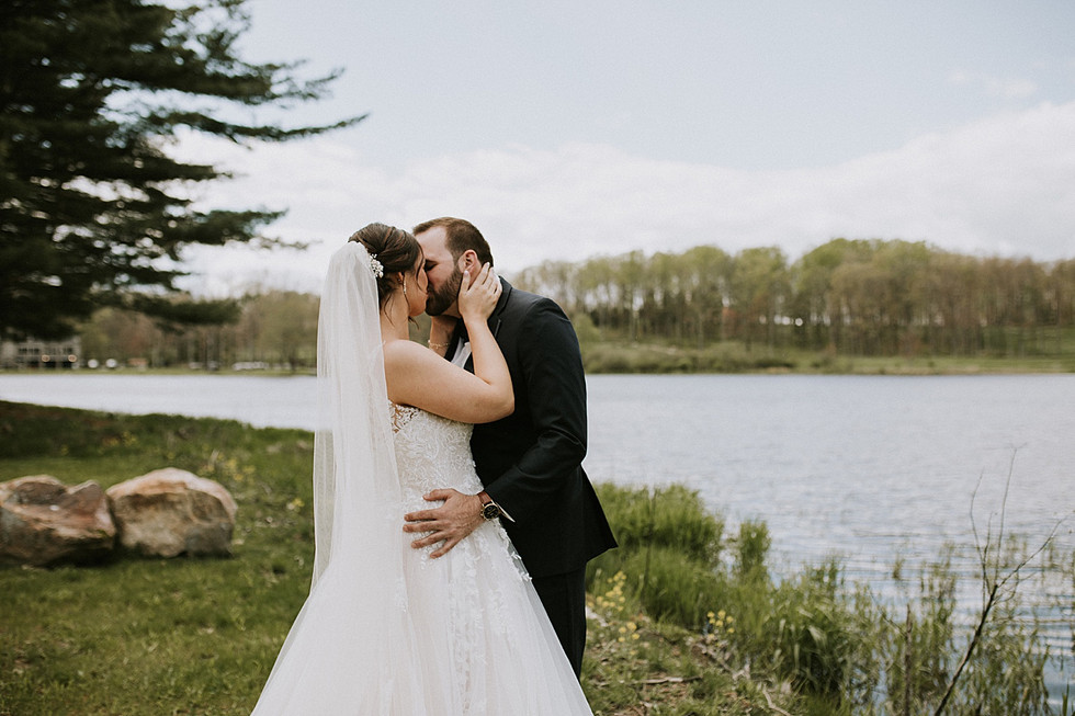 Bride and groom kiss during wedding portraits beside lake at Nemacolin Resort