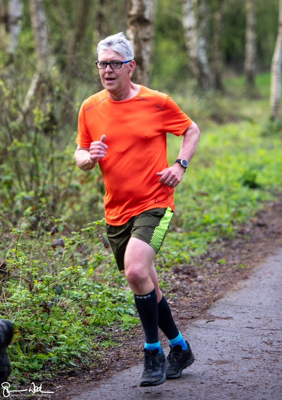 A man in an orange tshirt and black shorts running on a countryside path