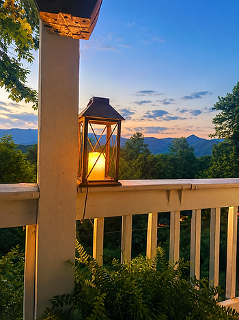 Lantern glowing on a mountain porch at dusk overlooking the Blue Ridge Mountains after a day of cleaning and reflection.
