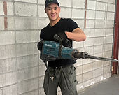 コンクリート壁の前で電動工具を持つ作業服姿の男性