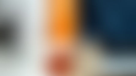 Two puzzle pieces, red and silver, connected on a desk with a laptop. Blurred orange object and phone in the background.