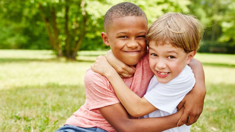 Two kids hugging each other in a park smiling