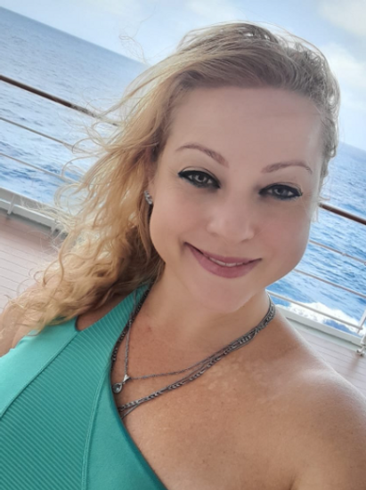 Mulher sorrindo serenamente, com o mar ao fundo e o vento nos cabelos, expressando liberdade, conexão interior
