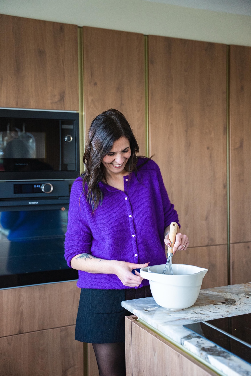 Jenny prépare une recette dans sa cuisine, en gilet violet