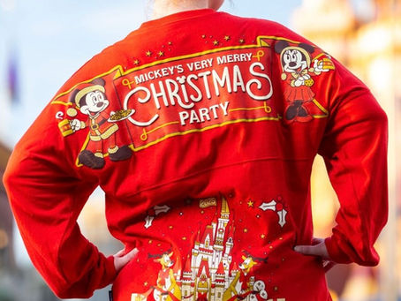 Person in red sweater with "Mickey's Very Merry Christmas Party" text, featuring Mickey and Minnie, stands in front of a blurred theme park.