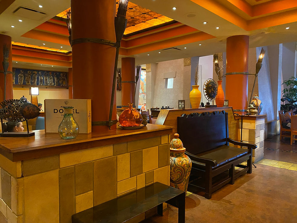 Warmly lit restaurant interior with orange columns, decorative pottery, and seating. Box with "Don Julio" tequila is visible on the counter.