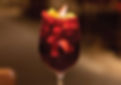 A glass of red sangria filled with ice, orange slices, and strawberries against a blurred, warm-toned background. Refreshing and vibrant.