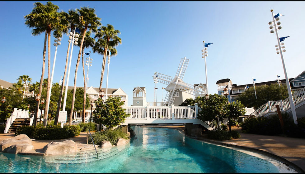 Palm trees and a windmill overlook a serene pool. White bridge connects gardens, with blue sky enhancing a tranquil resort atmosphere. This is stormalong bay at Disney's Beach Club.