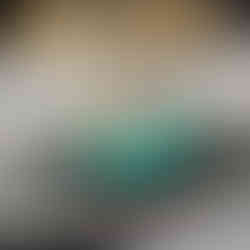 A turquoise dessert with a clock design on top sits on a decorative plate, with a blurred gold and dark blue background.