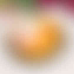 A tart with orange filling adorned with pink frosting, white flower, colorful sprinkles, and a character on a white disc. Pink flowers in background.