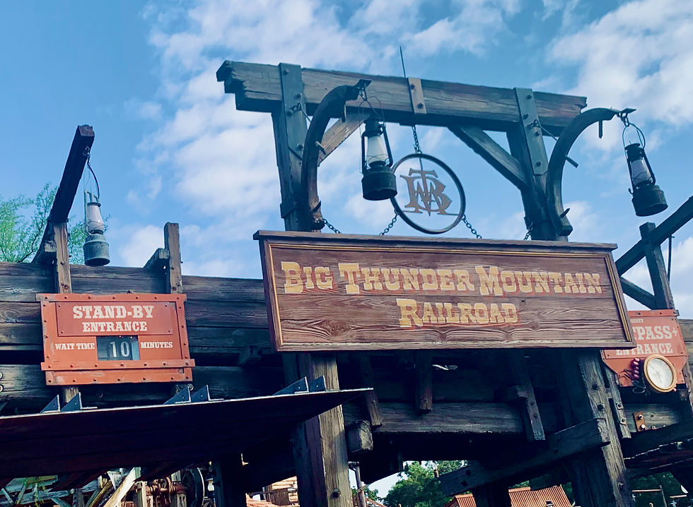 Big Thunder Mountain Railroad entrance with a rustic wooden sign and lanterns. Stand-by entrance shows 10-minute wait. Blue sky above Big Thunder Mountain Railroad at Magic Kingdom.
