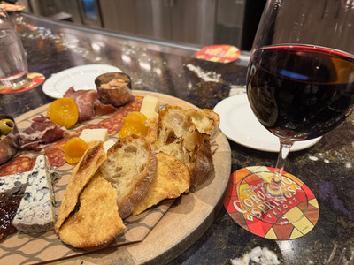Charcuterie board with cheese, meats, and bread on a table. A glass of red wine sits on a "Coronado Springs Resort" coaster nearby.