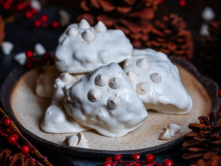 White meringue cookies on a plate surrounded by pinecones and red berries. Dark, festive background. No visible text. Cozy mood.