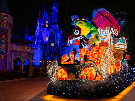 Festive parade float with vibrant colors, featuring a skeleton character playing guitar, colorful creature, lights, and castle backdrop at night.