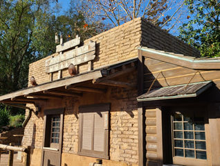 Rustic wooden building labeled Golden Oak Outpost, with closed sign. Set in a tree-lined area, under a clear blue sky.