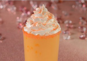 Orange milkshake with whipped cream and sprinkles in a pink setting. Background sparkles create a festive mood.