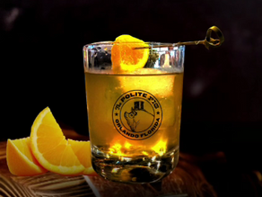 A cocktail in a glass with an orange slice and cherry on a skewer. "The Polite Pig Orlando Florida" logo. Dark background, orange slices nearby.