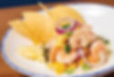 Shrimp ceviche with pineapple, red onion, jalapeños, and yellow peppers on a white plate. Garnished with tortilla chips. Bright, fresh setting.