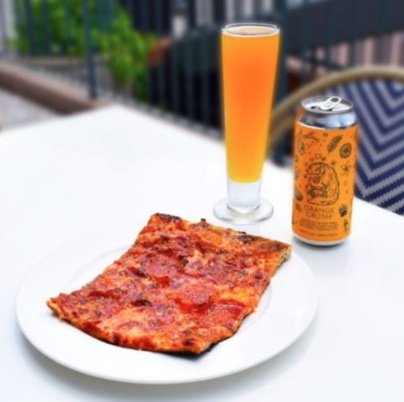 Slice of pepperoni pizza on a white plate, an orange drink in a glass, and a can labeled Orange Crush on an outdoor table.