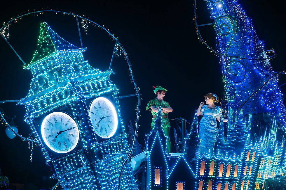 Two people in costume smile atop a float with bright blue fairy lights and clock tower design at night. Enchanting and festive atmosphere.