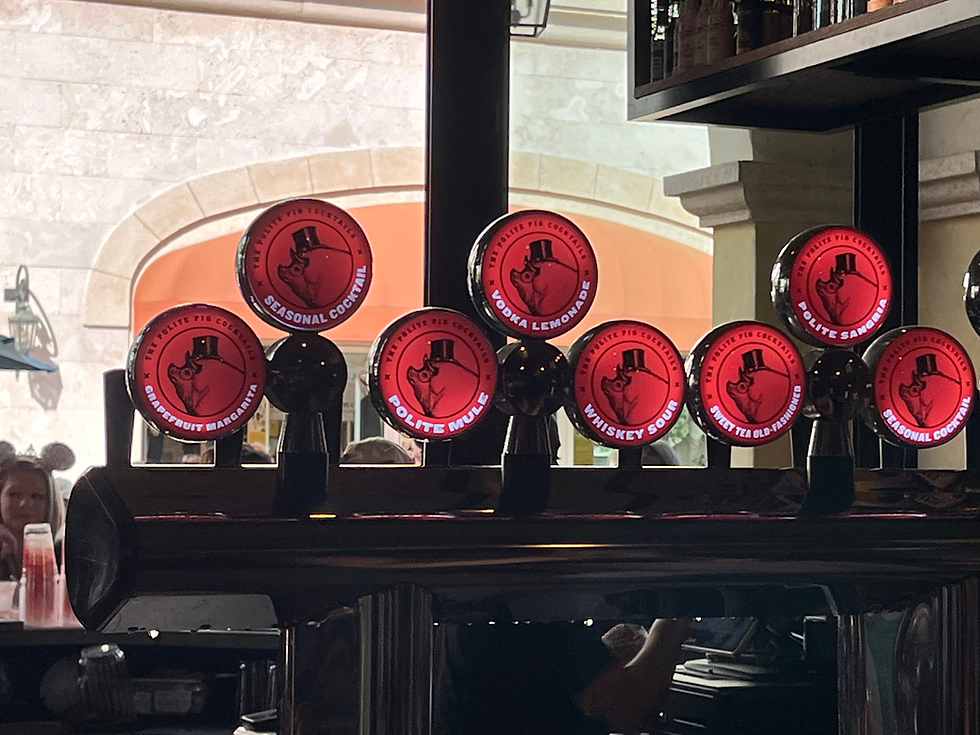 Red beer taps at a bar with labels like Vodka Lemonade and Polite Mule. Background shows arched windows and wall. Dim lighting. This at at The Polite Pig at Disney Springs.